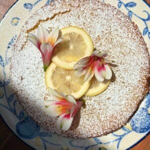 This image shows a Lemon & Olive Oil cake decorated with lemon wedges and flowers.